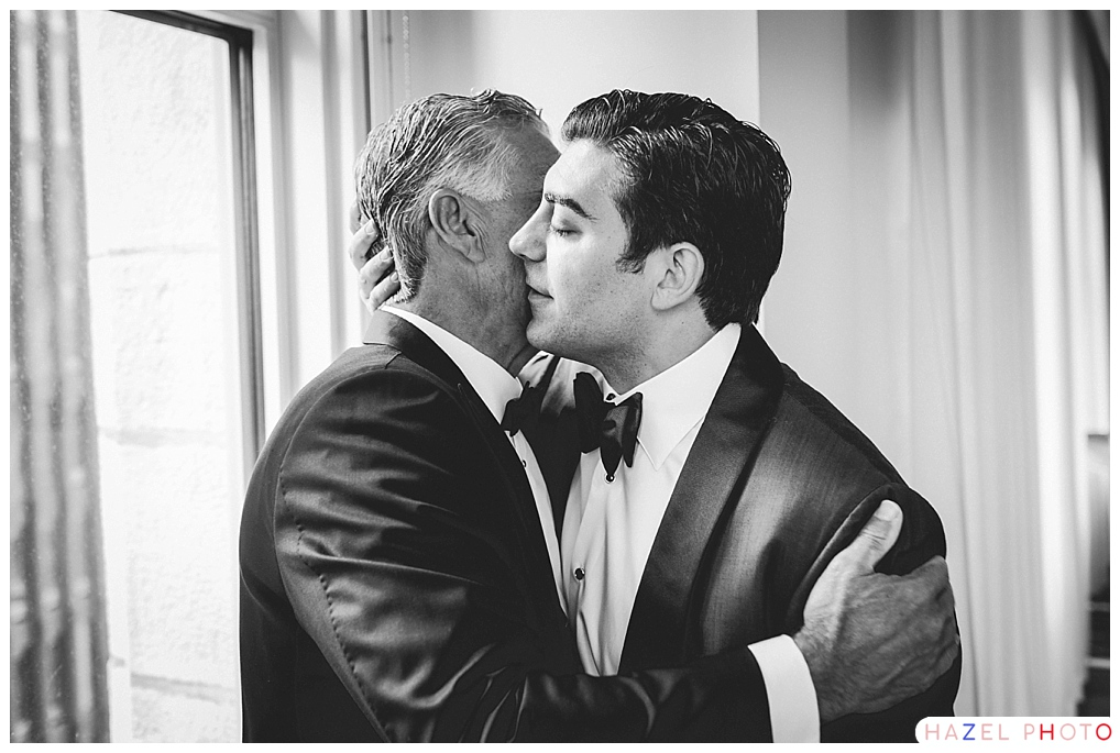 a groom and his father share a hug at the hotel before heading over to the church for the wedding. Documentary wedding photography